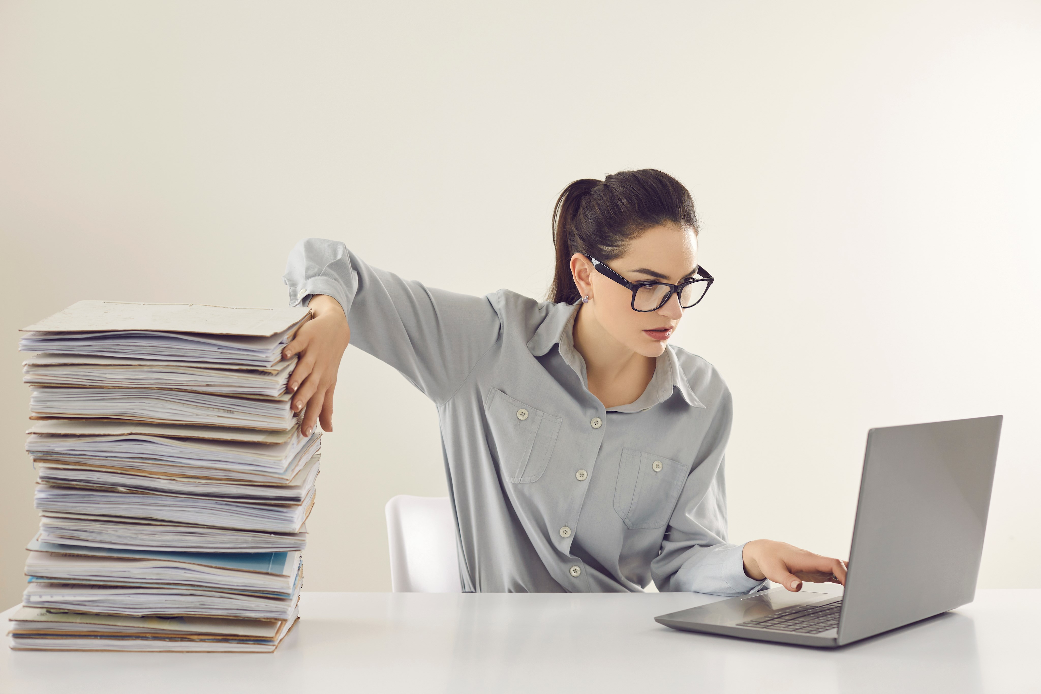 Frau vor Laptop mit Aktenstapel